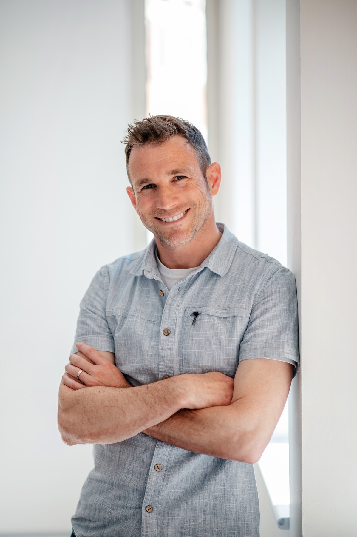Jono Hey smiling with arms folded, leaning against a white wall